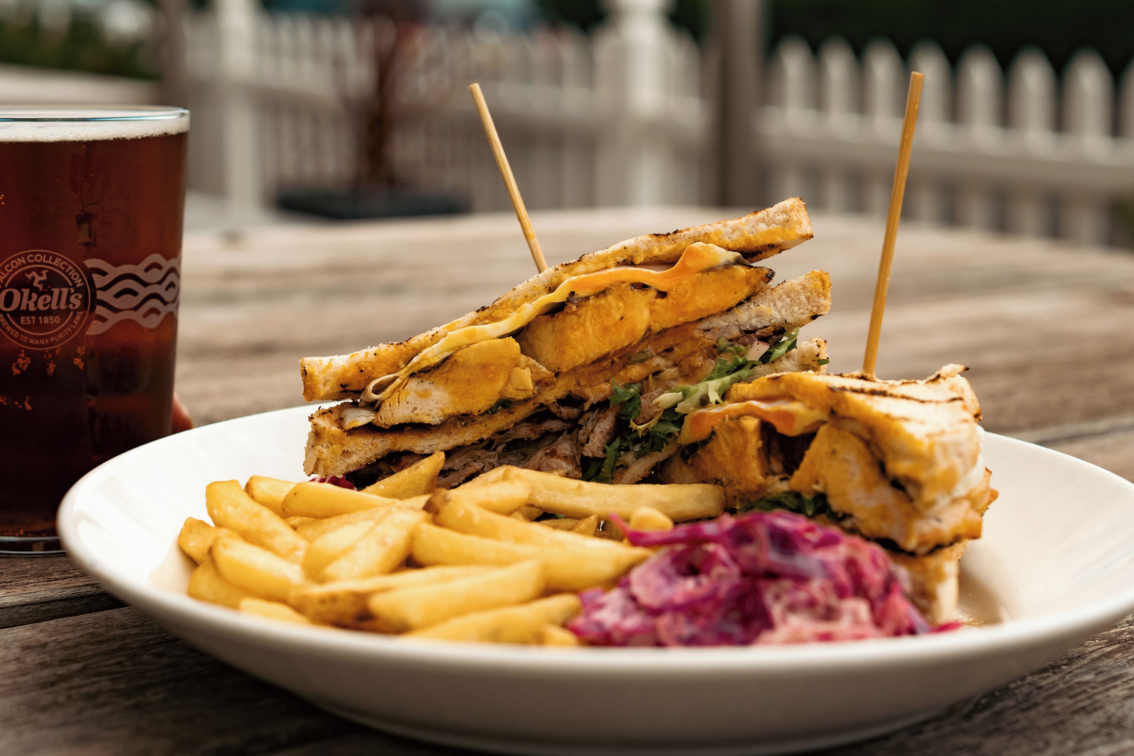 A sandwich with a side of fries and coleslaw on a plate, with a glass of beer in the background.