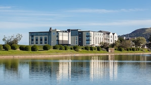 A modern multi-story hotel with a flat roof, located beside a calm lake.