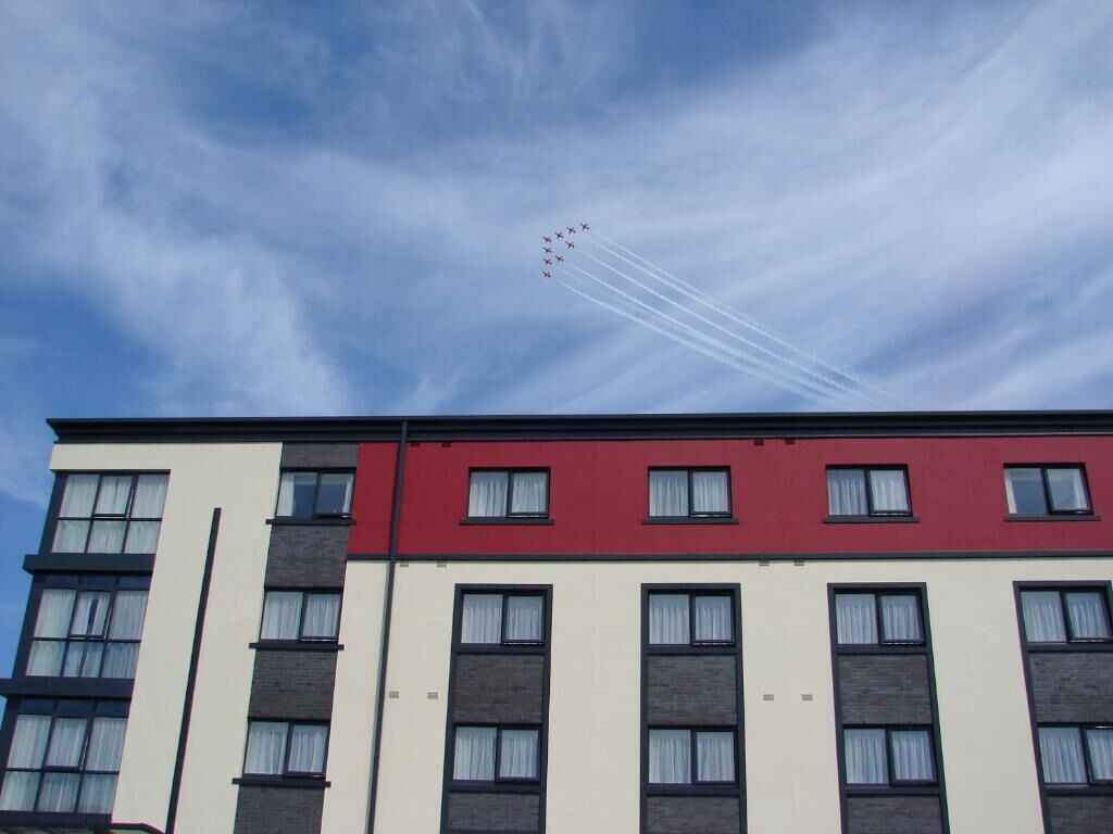 Een meerlaags gebouw met een gevel in rood en wit, meerdere ramen en een heldere lucht met spoorvliegtuigen.