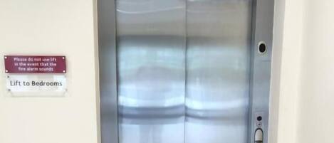 A metallic elevator with a digital display showing the number 2. There is a sign on the wall that reads "Please do not use lift in the event that the fire alarm sounds" and "Lift to Bedrooms".