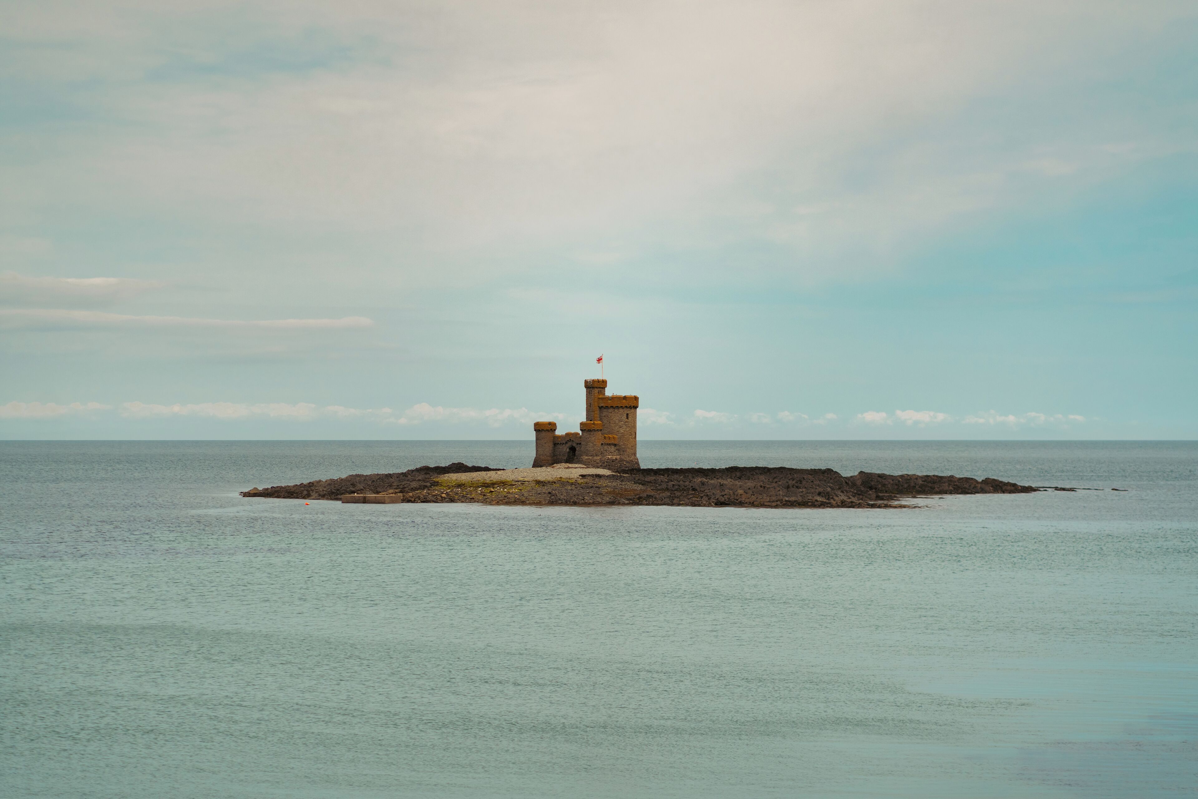A lighthouse on a small island with calm water and a clear sky.