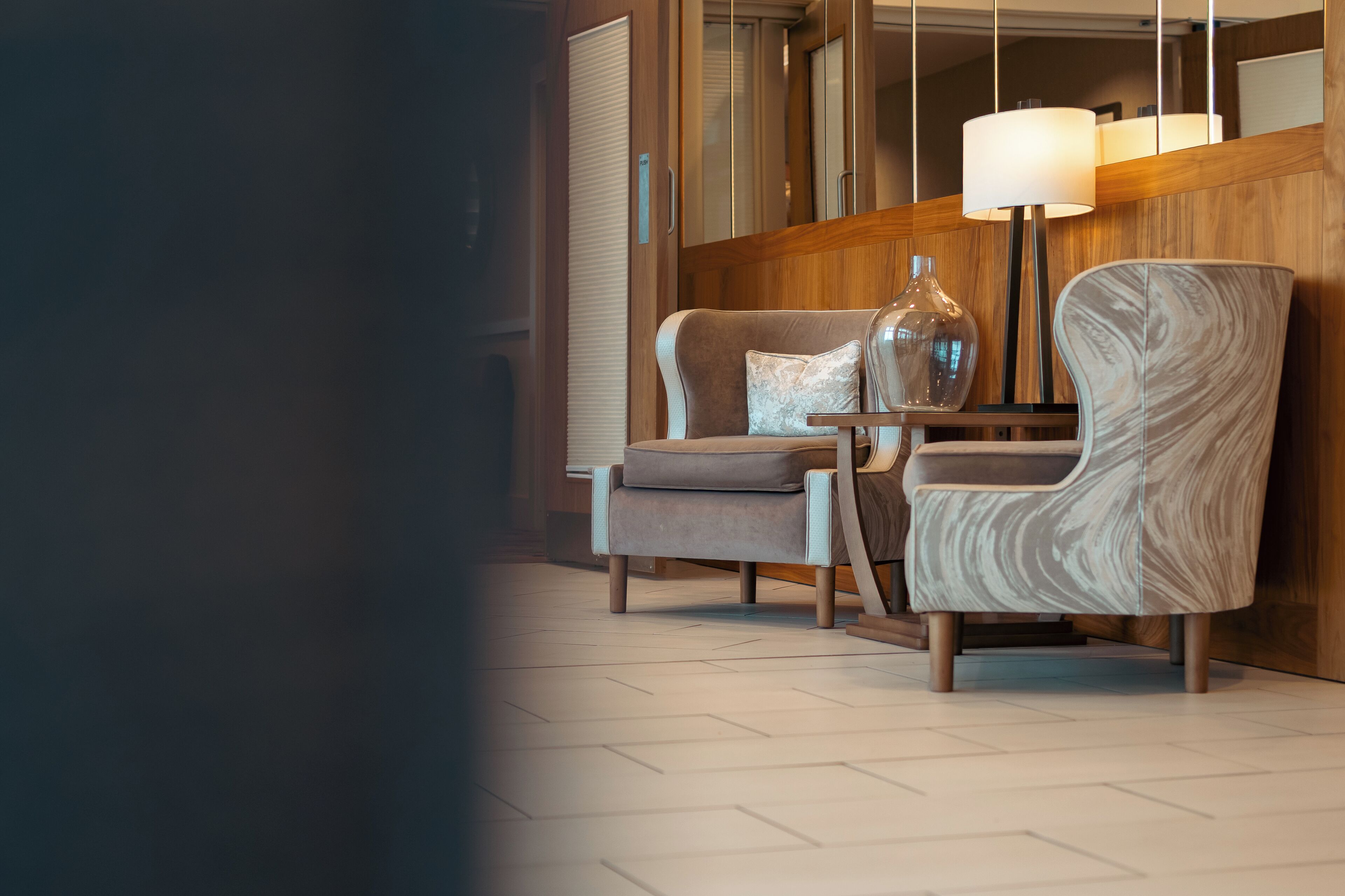Een moderne hotelkamer met een wand van houten panelen, een grote spiegel, een bank, een stoel en een vloerlamp.