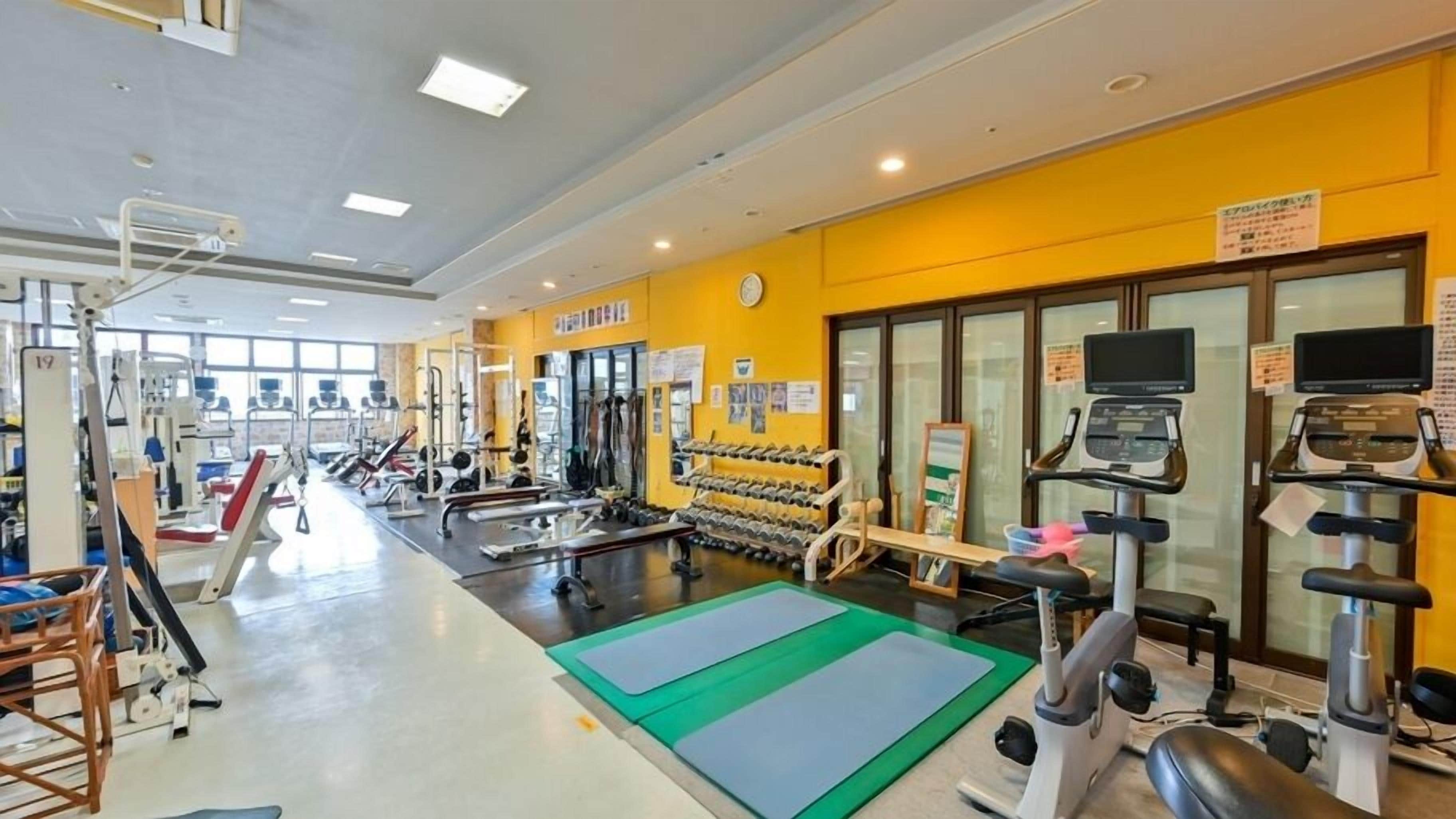 A gym with exercise equipment, weight racks, and a green mat area.