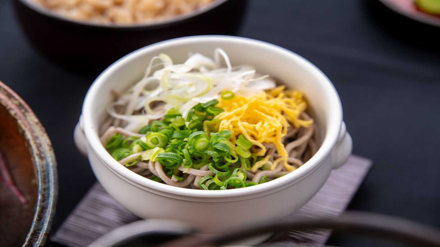 A bowl of noodles with green onions and shredded cheese.