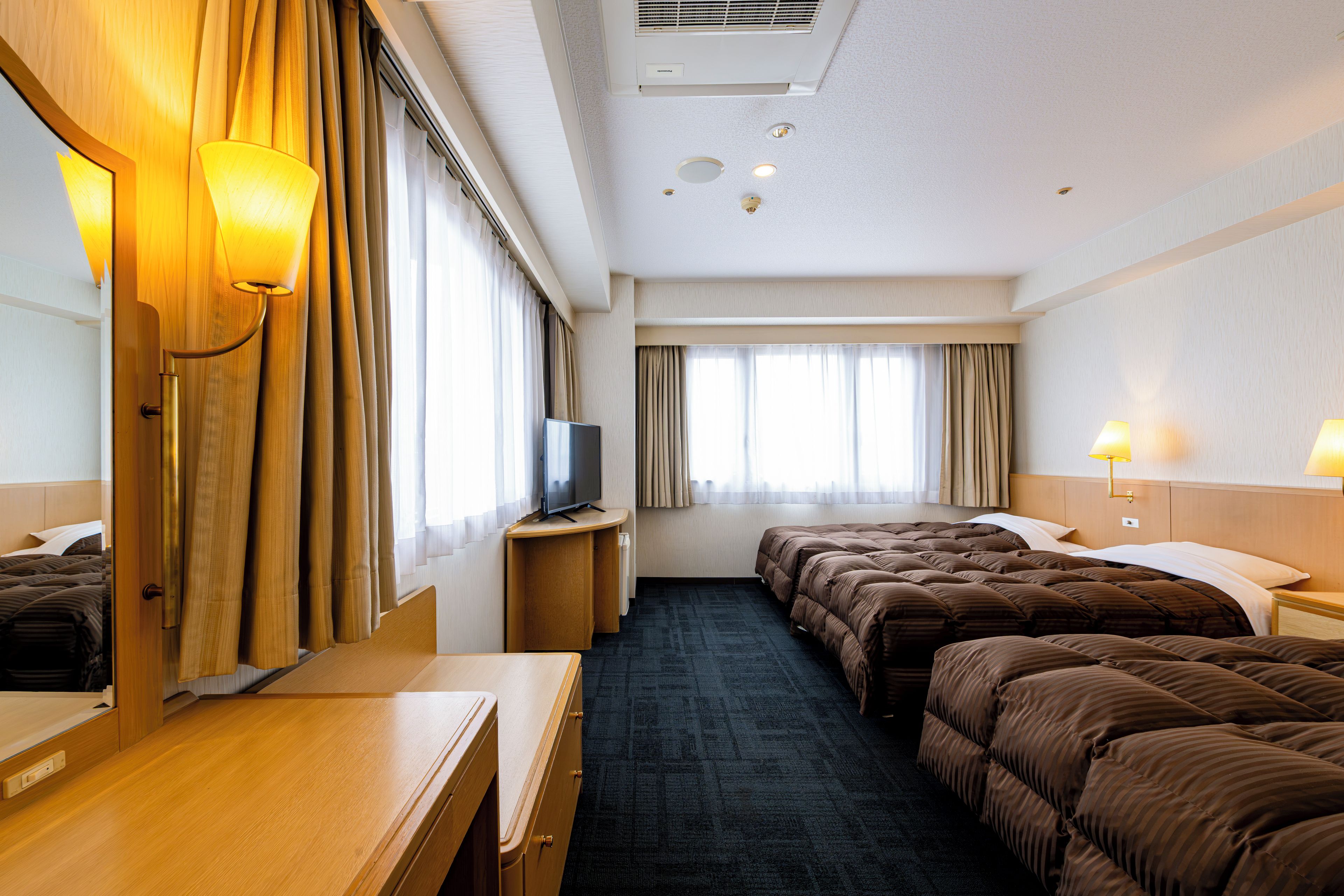 A hotel room with a bed, a desk, a television, and a window with curtains.