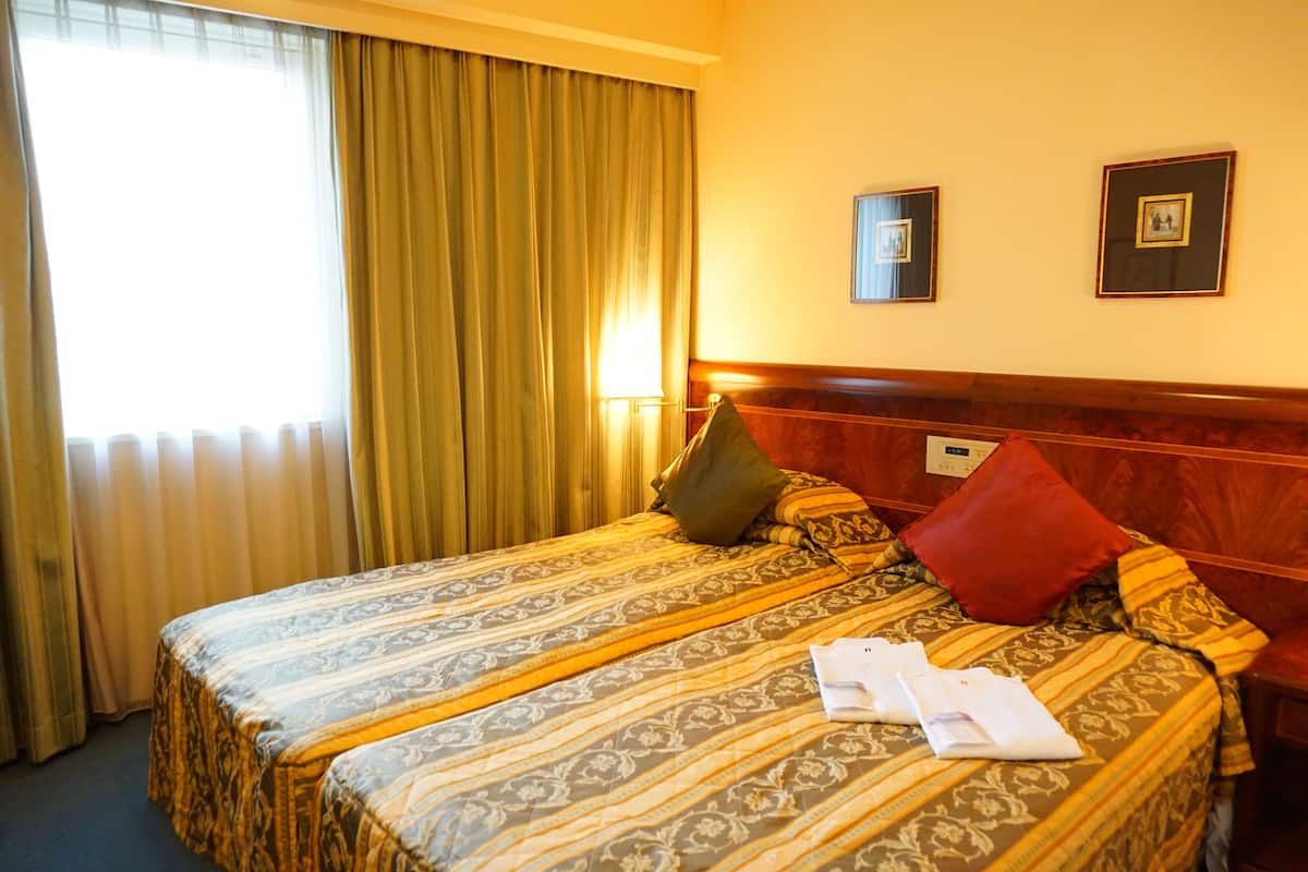 A hotel room with a large bed, a headboard, and a window with curtains.