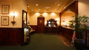 A hotel lobby with a reception desk, a large mirror, framed pictures on the wall, and a potted plant.
