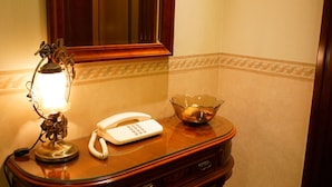 A wooden bedside table with a lamp, a telephone, and a glass bowl.