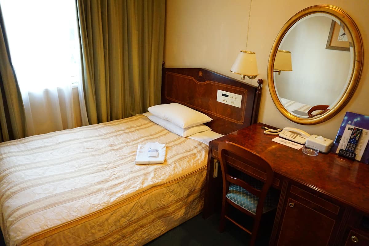 A hotel room with a bed, a bedside table with a lamp, a telephone, and a mirror.