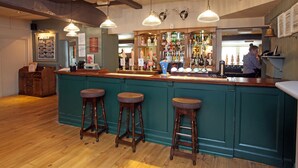 A bar area with wooden stools, a bar counter, and hanging pendant lights. - Original White Hart, Ringwood by Marston's Inns (Ringwood)