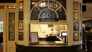 A reception area with a sign reading "Reception" above a desk, surrounded by stained glass windows. - Original White Hart, Ringwood by Marston's Inns (Ringwood)