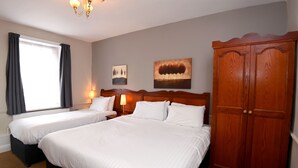 A hotel room with two beds, a wardrobe, a window with curtains, and two wall-mounted lamps. - Original White Hart, Ringwood by Marston's Inns (Ringwood)