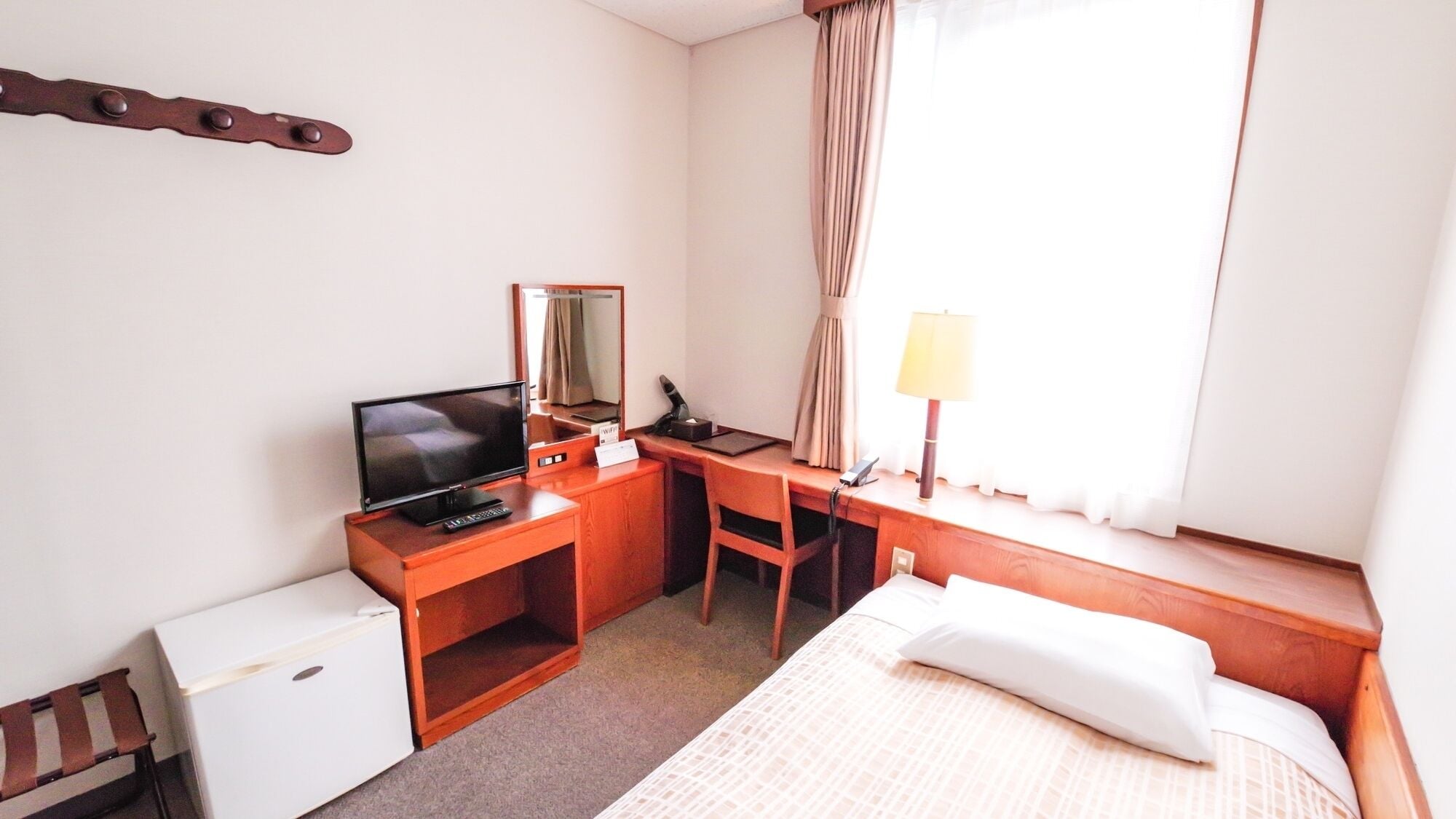 A hotel room with a bed, a desk with a computer, a television, a lamp, and a small refrigerator.