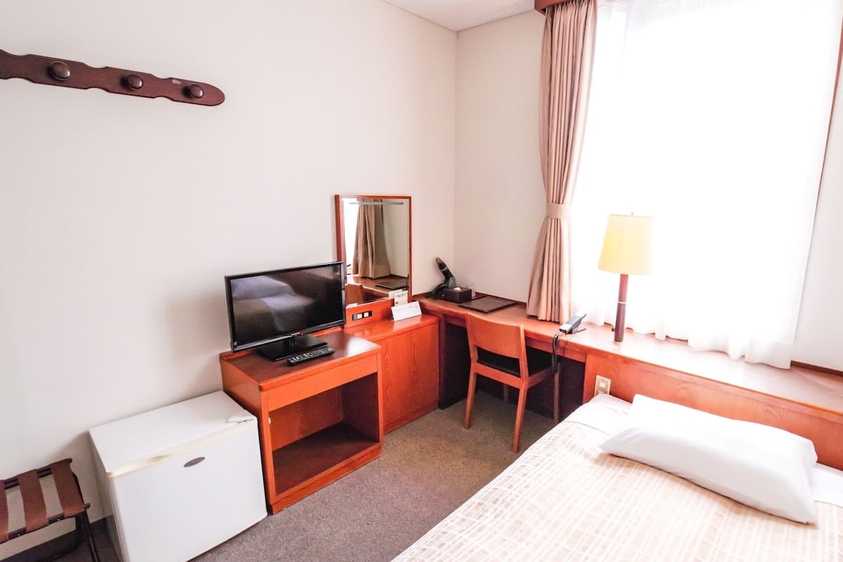 A hotel room with a bed, a desk with a computer, a television, a lamp, and a small refrigerator.