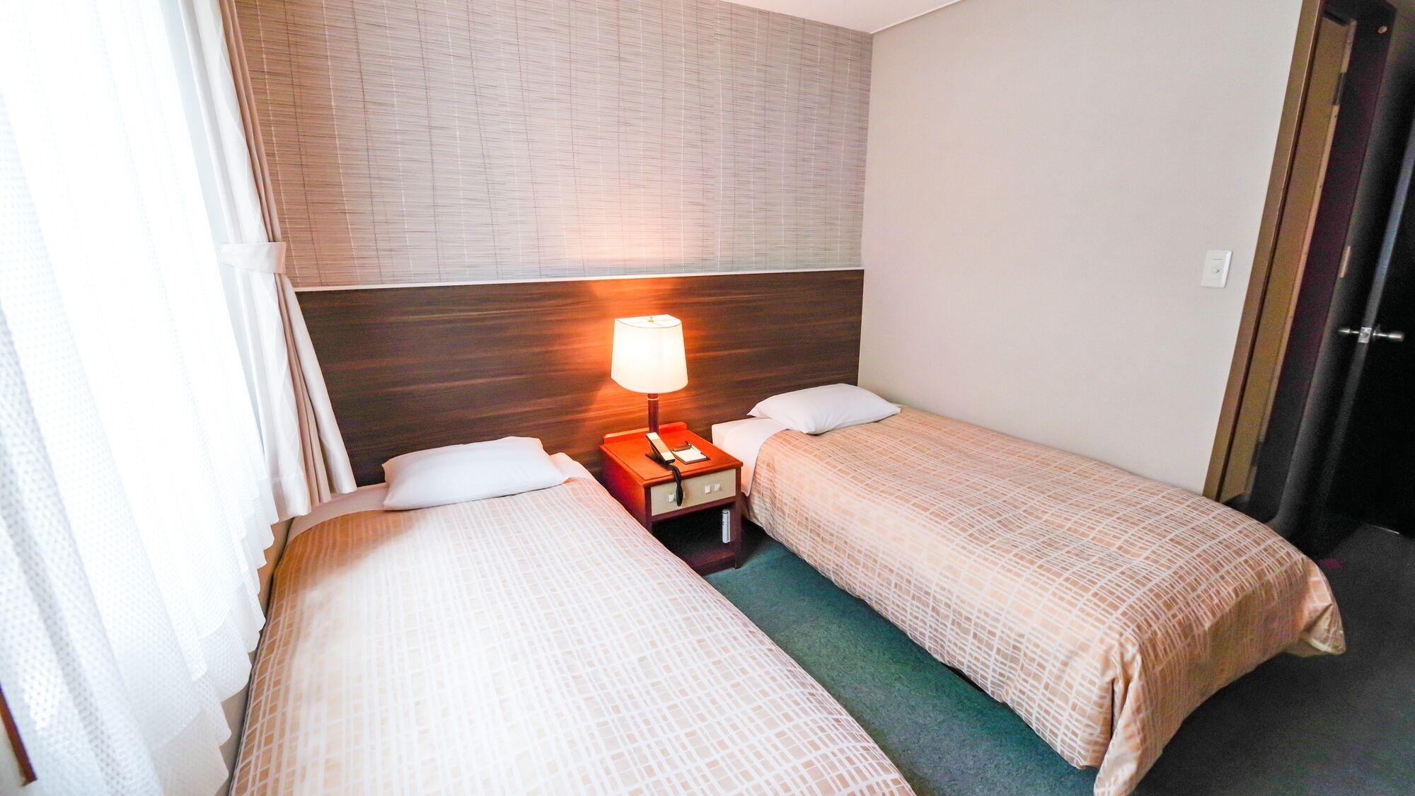 A hotel room with two single beds, a nightstand with a lamp, and a door to the right.