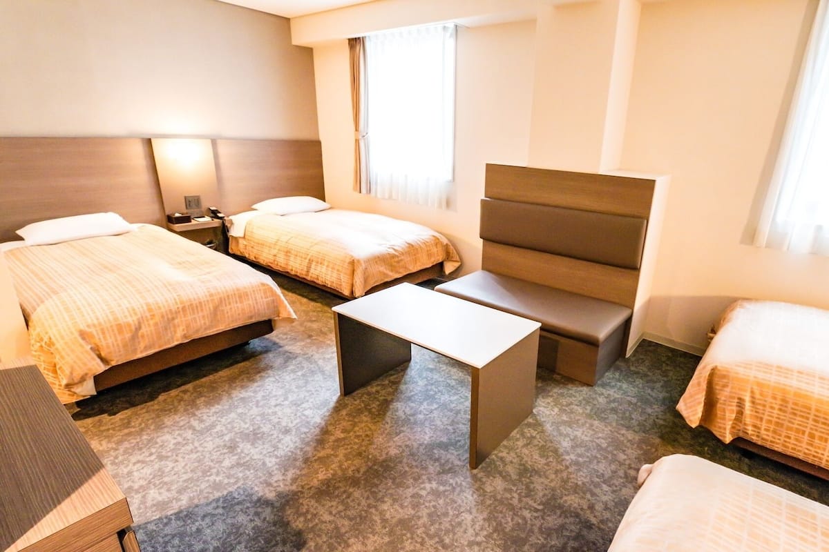 A hotel room with two beds, a sofa, a small table, and a nightstand.