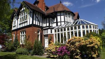 Una casa de estilo Tudor con un invernadero, rodeada de jardines cuidados.