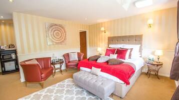 Habitación de hotel con una cama grande, una decoración en tonos rojo y blanco, un banco gris, un sillón de cuero rojo, una mesita auxiliar pequeña y una lámpara de pared.