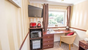 A compact room with a desk, a chair, a television, a microwave, and a small refrigerator. - Norman Hurst (Sale)
