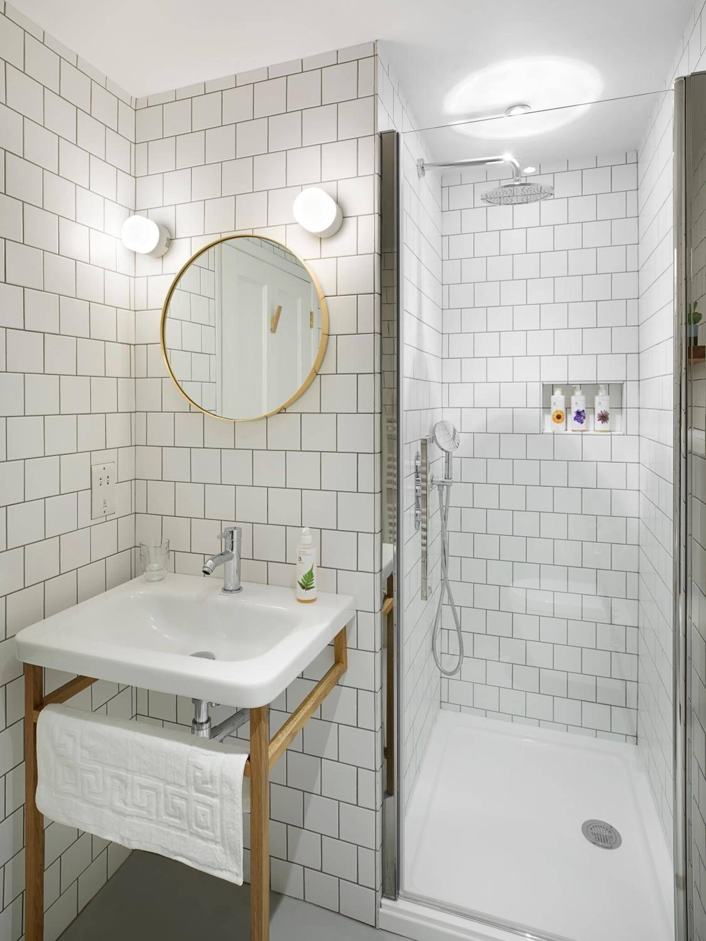 A bathroom with a white tiled shower, a sink with a mirror, and a towel hanging on the wall.