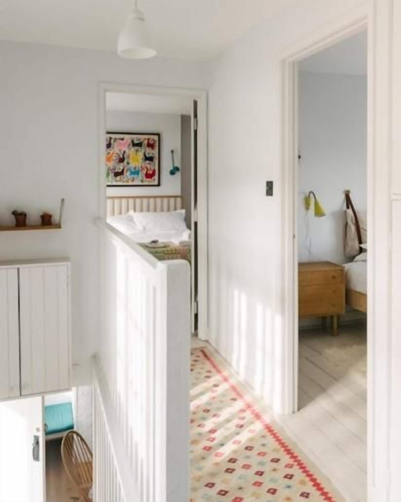 A narrow hallway with a white radiator, a wooden door, and a bed with a red and white patterned rug.