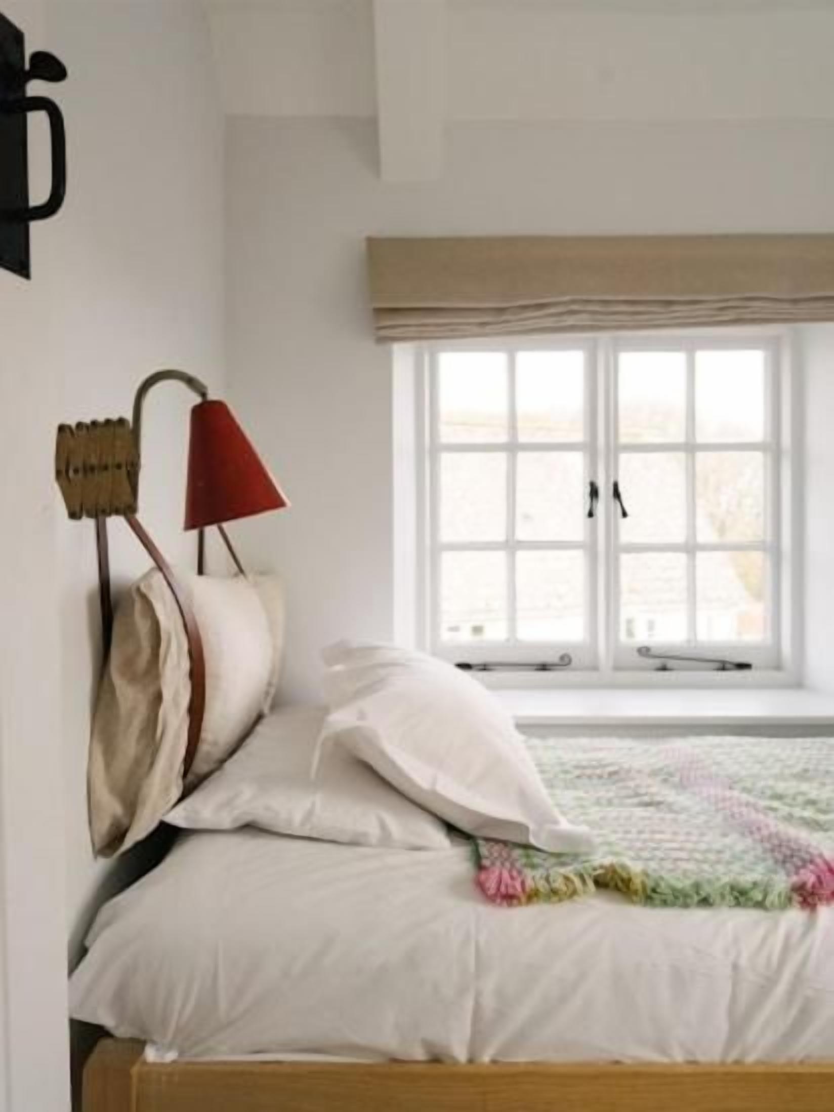 A bed with white linens, a red lamp, and a window with a view of the outdoors.