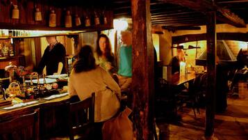 A rustic interior with wooden beams, a bar area with bottles, and a brick oven in the background.