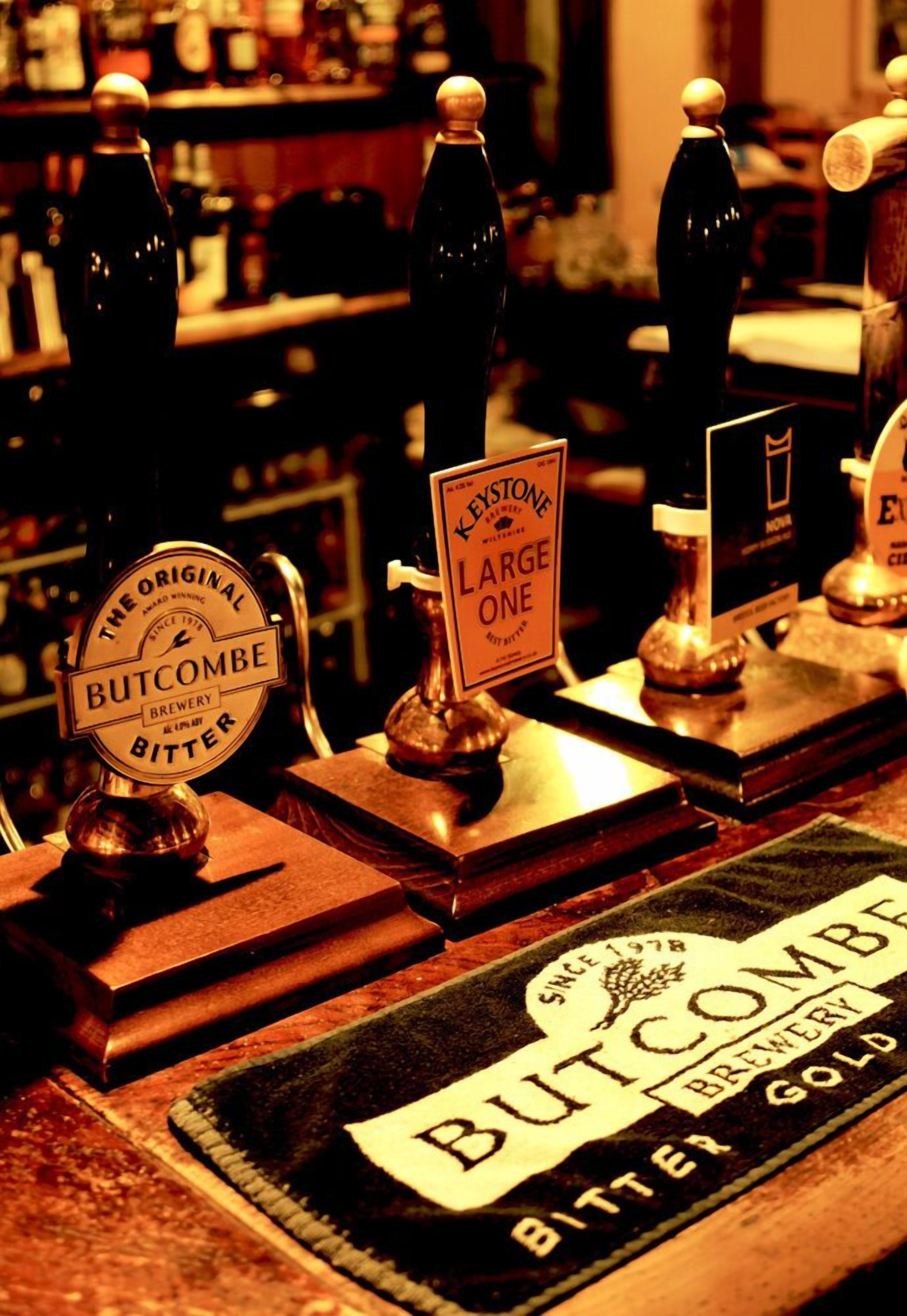 Een bar met meerdere biertappen, gelabeld 'Butcombe Brewery Bitter' en 'Keystone Large One'.
