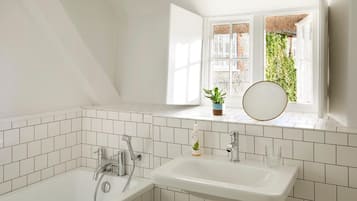 A modern bathroom with white tiles, a bathtub, a sink, a potted plant, and a mirror.