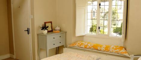 A bedroom with a bed, a dresser, a window with a view of greenery, and a door.