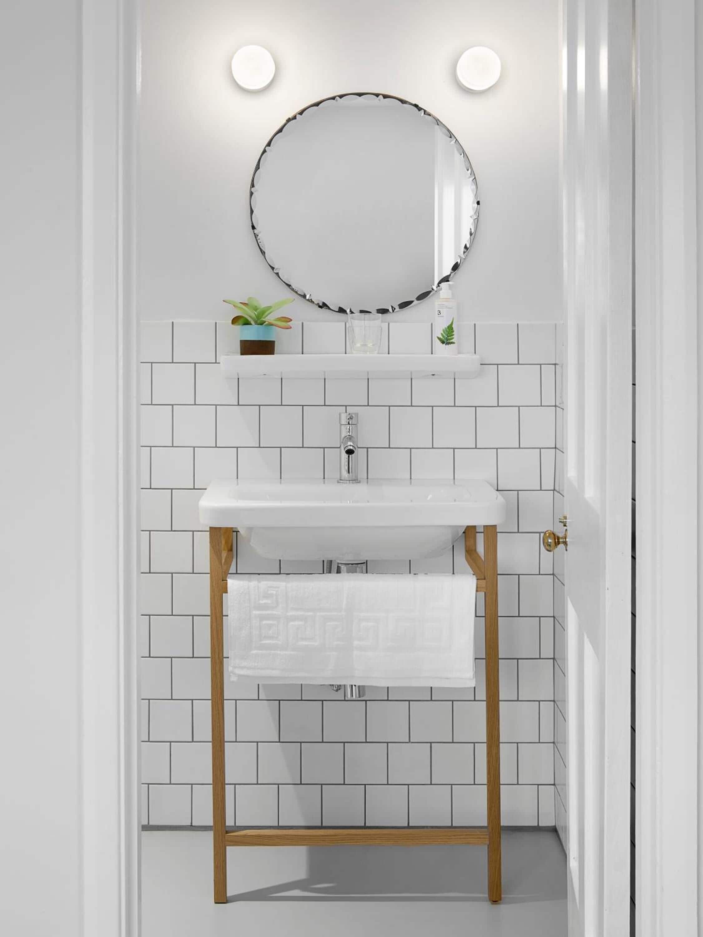 Un baño con un lavamanos blanco, un espejo redondo y una planta pequeña en la estantería.