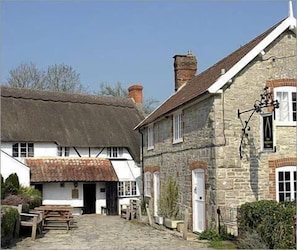 A traditional stone building with a thatched roof and a wooden bench in the courtyard.