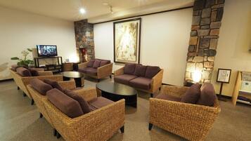 A lounge area with wicker furniture, a stone wall, and a television.