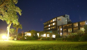 Un hôtel à plusieurs étages, dont les fenêtres sont illuminées, entouré de pelouses et d’arbres bien entretenus.