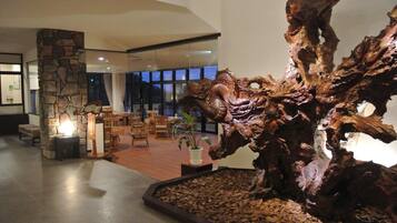 Una hall con una grande scultura in legno, un pilastro in pietra e una zona con posti a sedere.