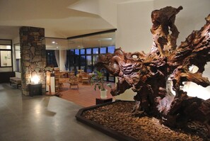 Un hall d’entrée agrémenté d’une grande sculpture en bois, d’un pilier en pierre et d’un espace détente avec des sièges.