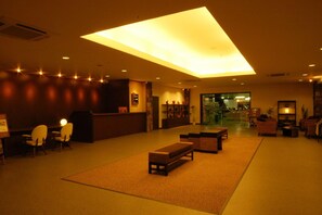 Un hall d’hôtel comprenant un comptoir d’accueil, un espace salon et une grande verrière.