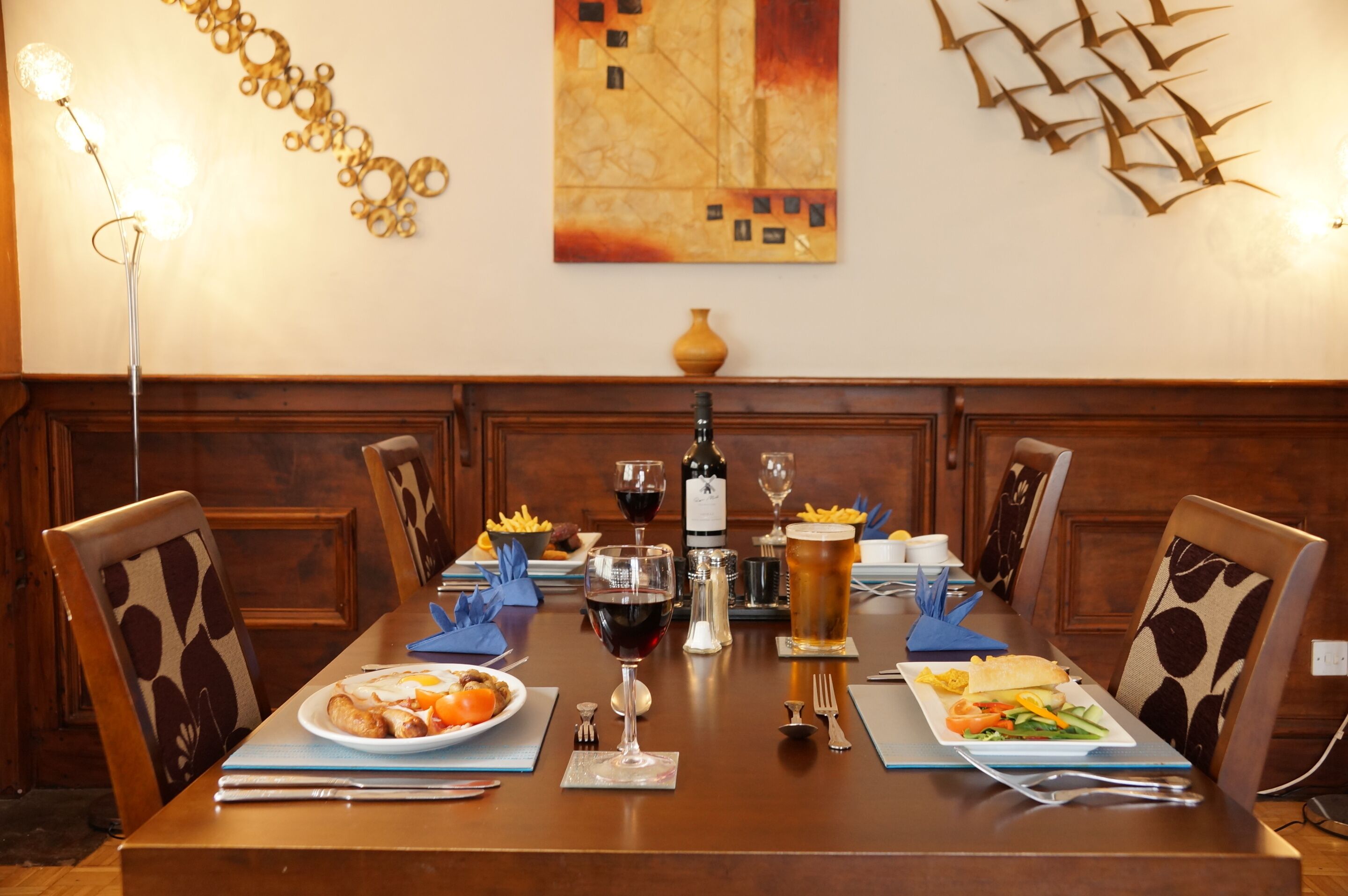 Una mesa de comedor dispuesta con platos de comida, copas de vino y una jarra de cerveza.