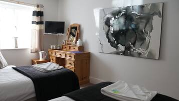 A bedroom with two beds, a wooden dresser, a flat-screen TV, a large abstract painting, and a window with curtains.
