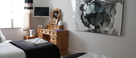 A bedroom with two beds, a wooden dresser, a flat-screen TV, a large abstract painting, and a window with curtains.