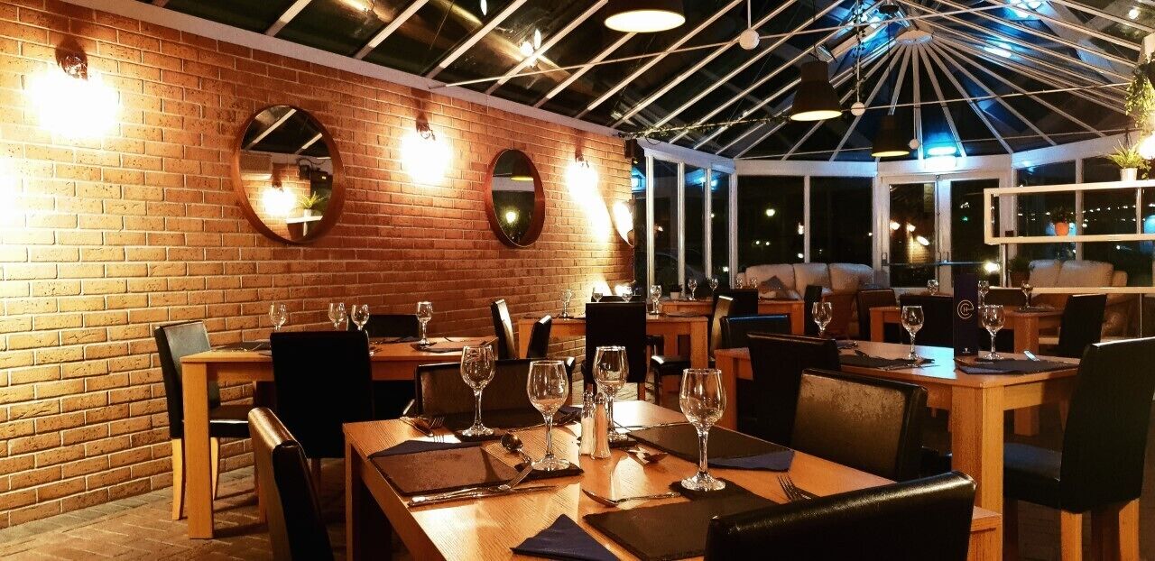 A restaurant with brick walls, round mirrors, and wooden tables set for dining.