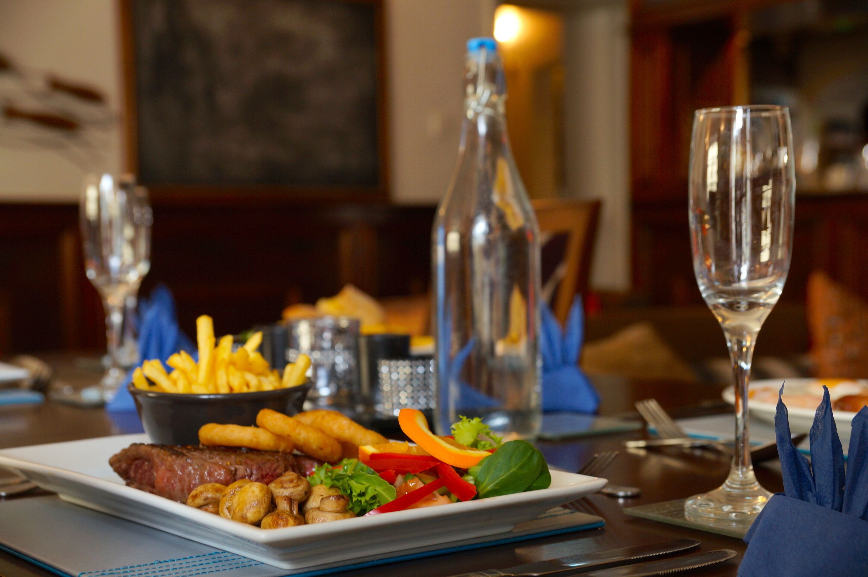A dining table with a plate of food, a bottle, and glasses.
