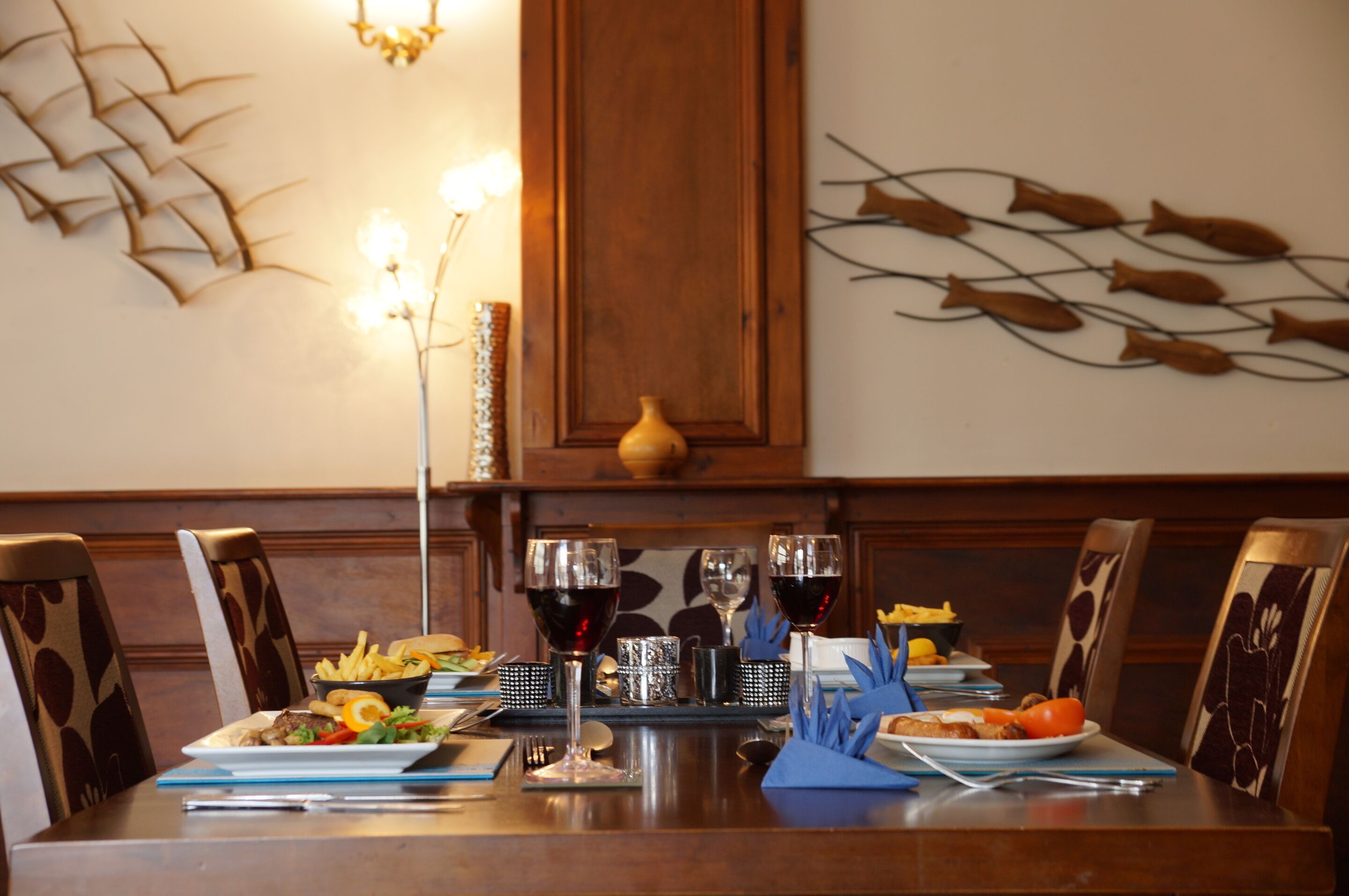 Une table à manger dressée avec des assiettes, des verres et des couverts, entourée de chaises dont les sièges sont recouverts d’un tissu à motifs.