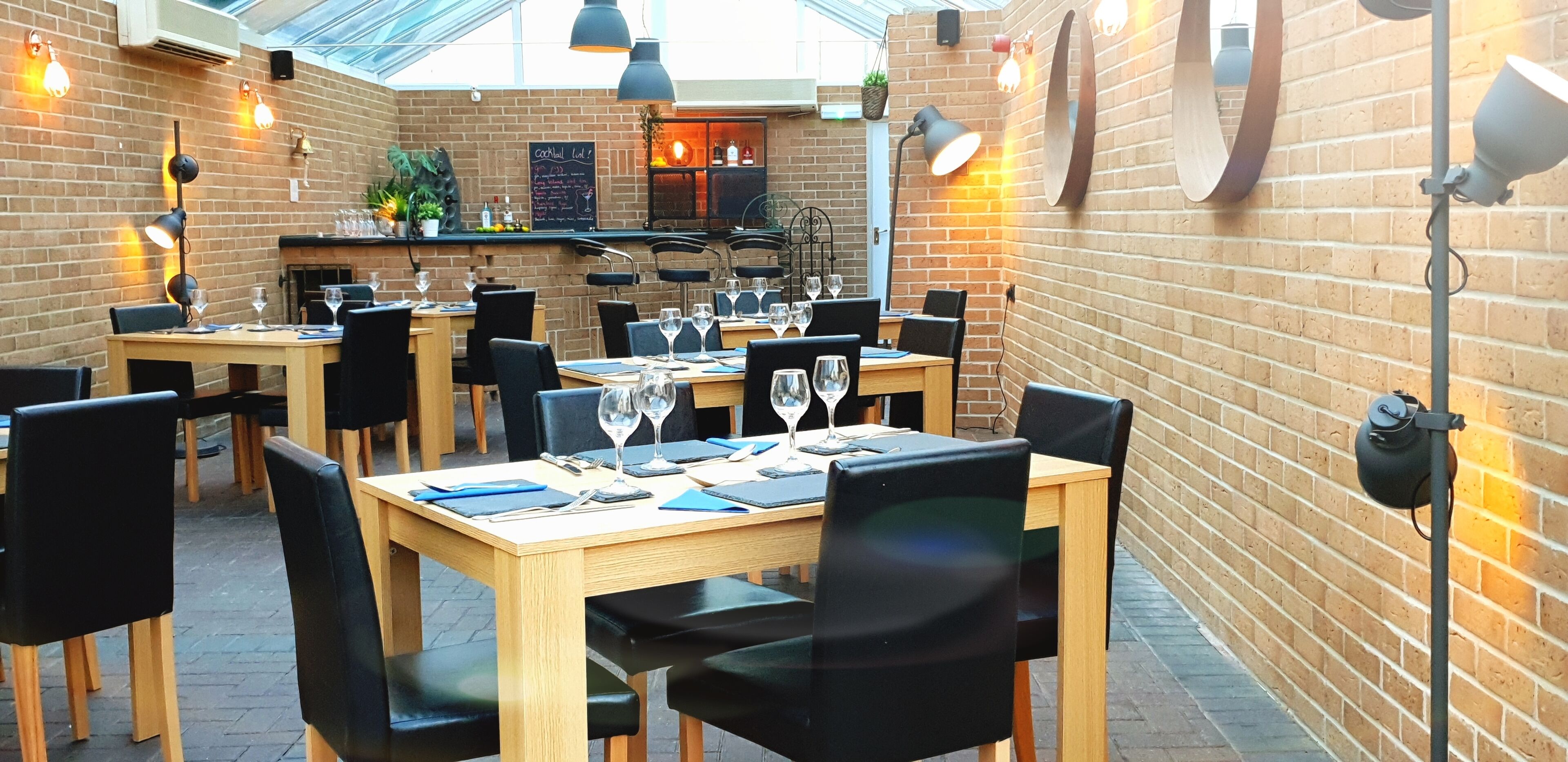 An indoor restaurant with brick walls, wooden tables, black chairs, and hanging pendant lights.