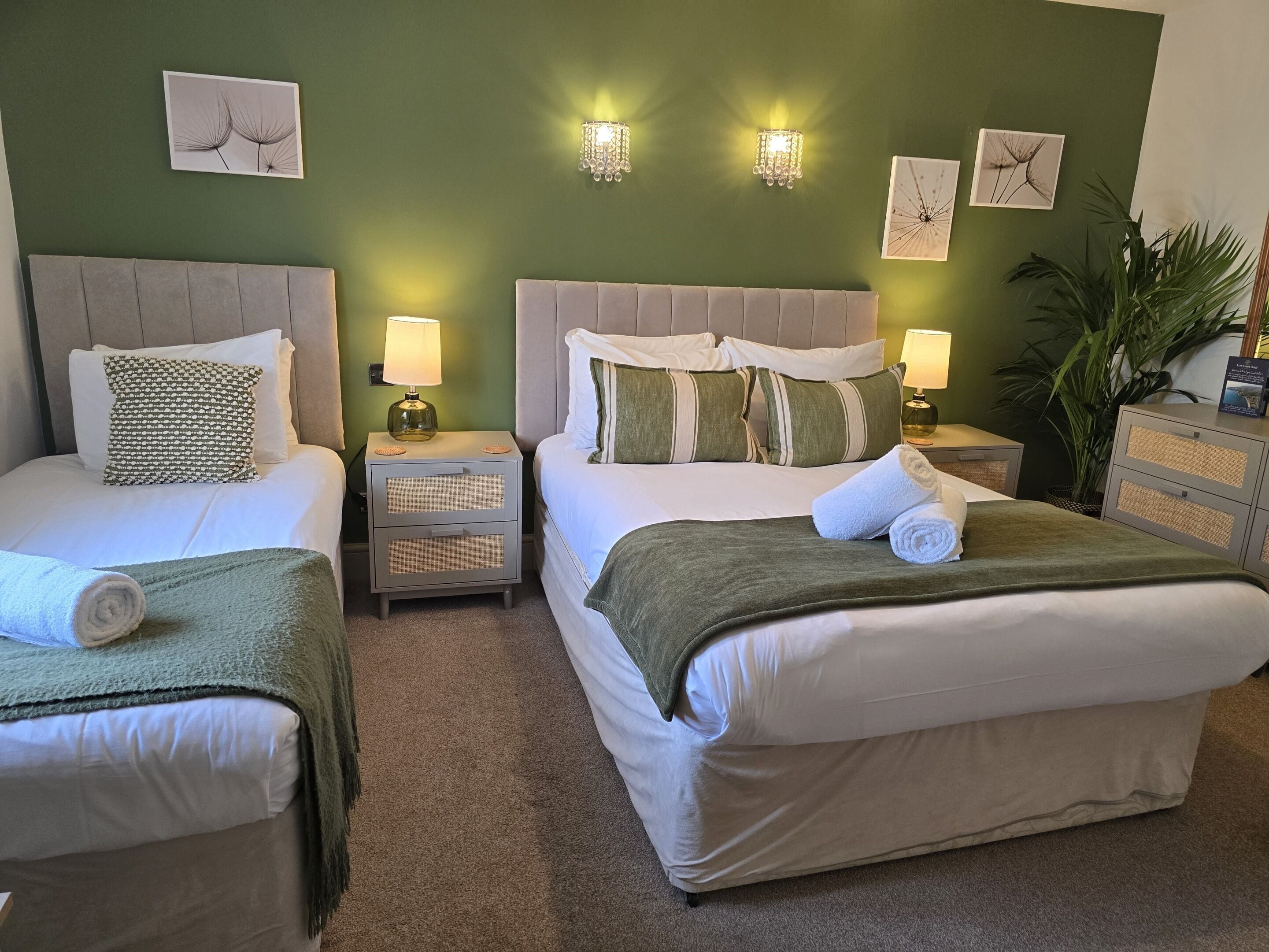 A hotel room with two beds, a nightstand with a lamp, and wall-mounted sconces.