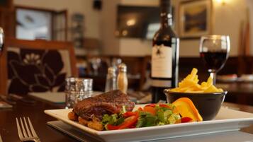 Una mesa de comedor con un plato de comida, una botella de vino y una copa de vino tinto.