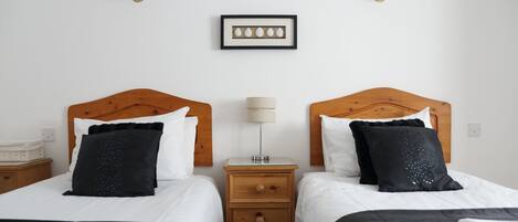Habitación de hotel con dos camas, cabecera de madera, mesita de noche con lámpara y un cuadro en la pared.