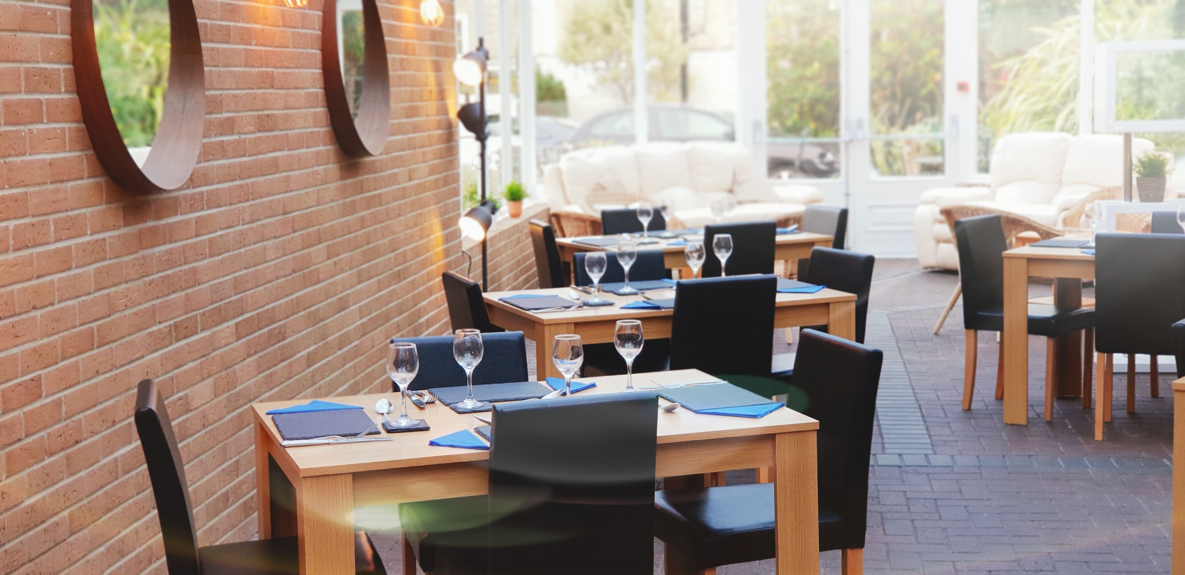 An outdoor dining area with brick walls, wooden tables, and black chairs.
