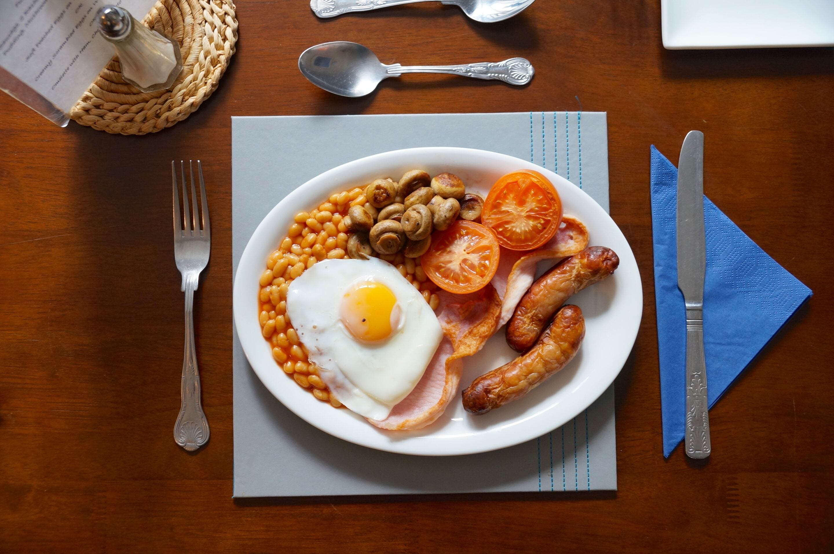 Un piatto di cibo per la colazione con uova, salsicce, pomodori e fagioli su un tavolo di legno.