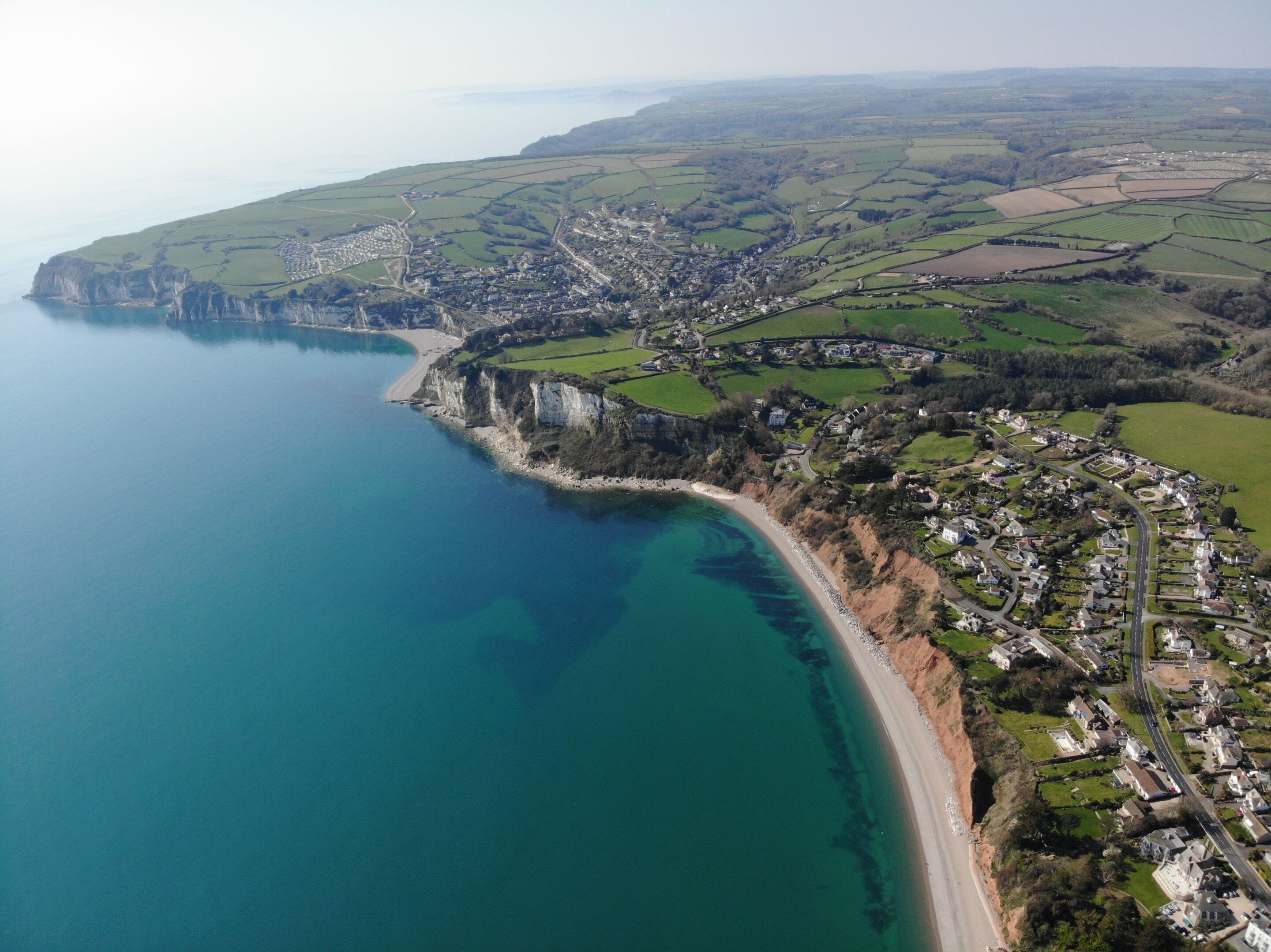 An aerial view of a coastal town with a beach, cliffs, and farmland.